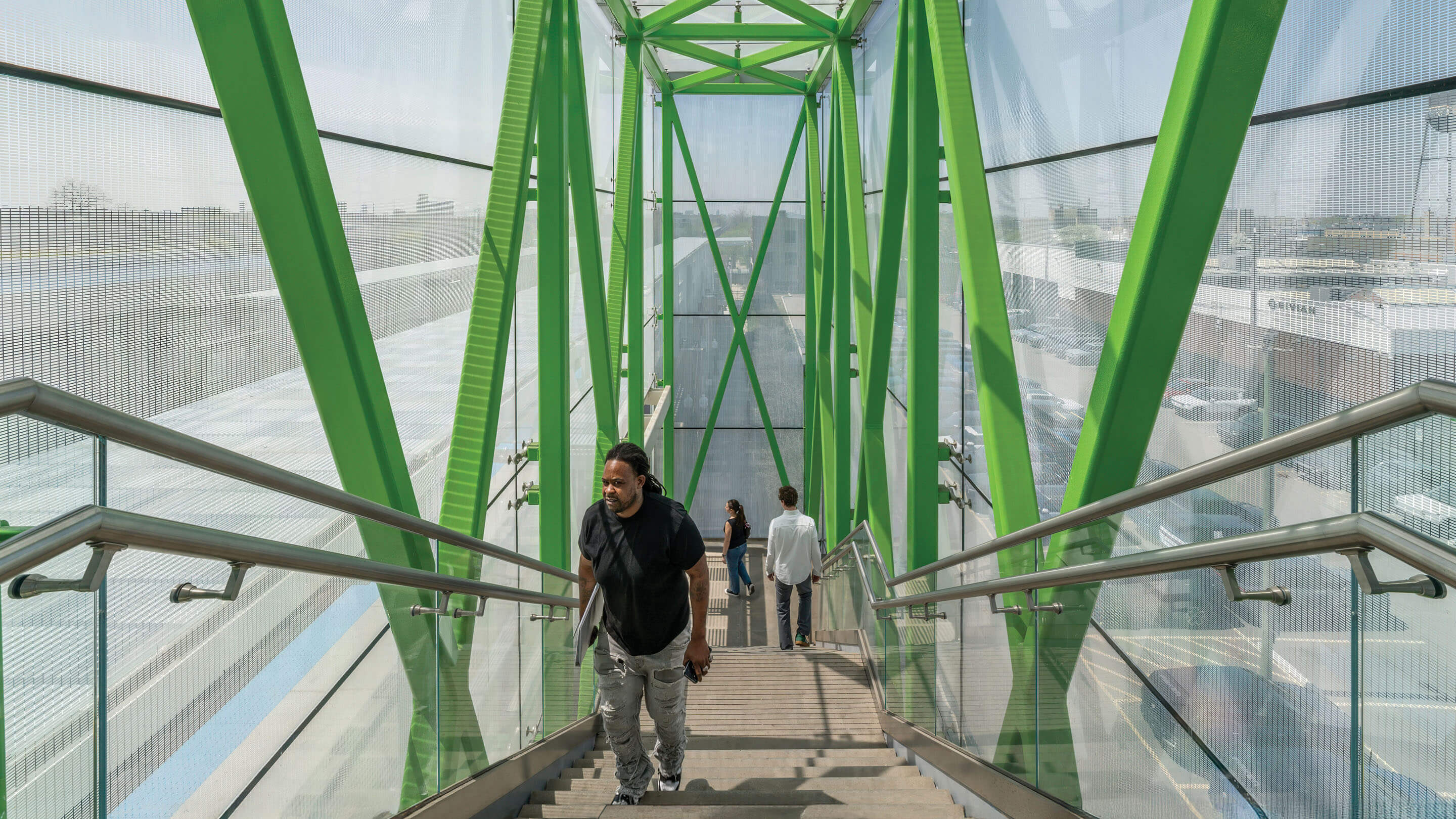 Modern green pedestrian bridge with people ascending in sunlight.