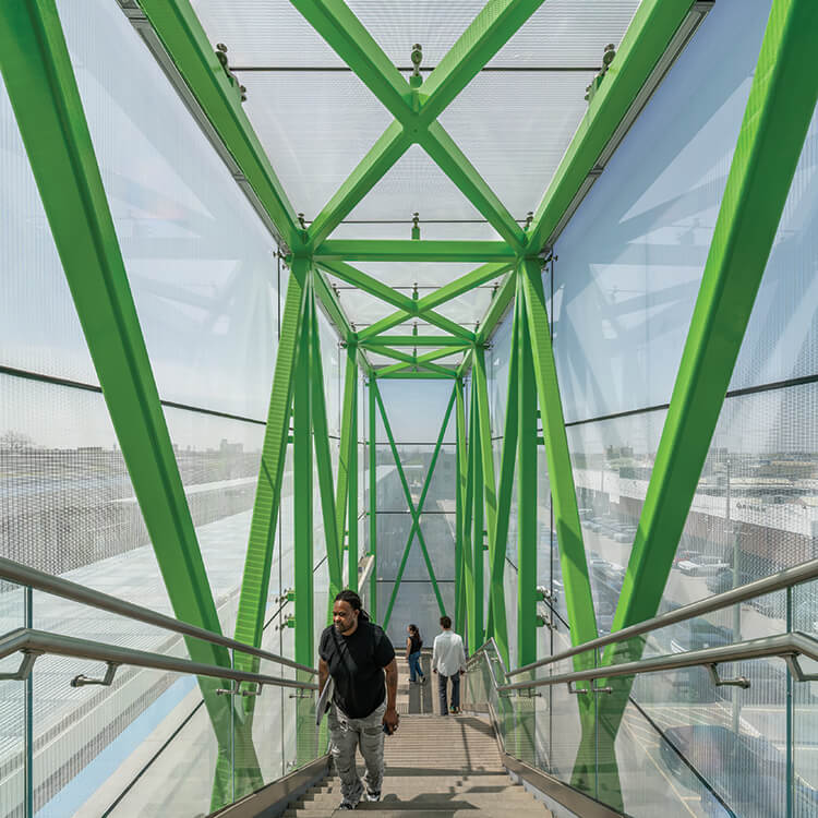 Modern green pedestrian bridge with people walking down the stairs.