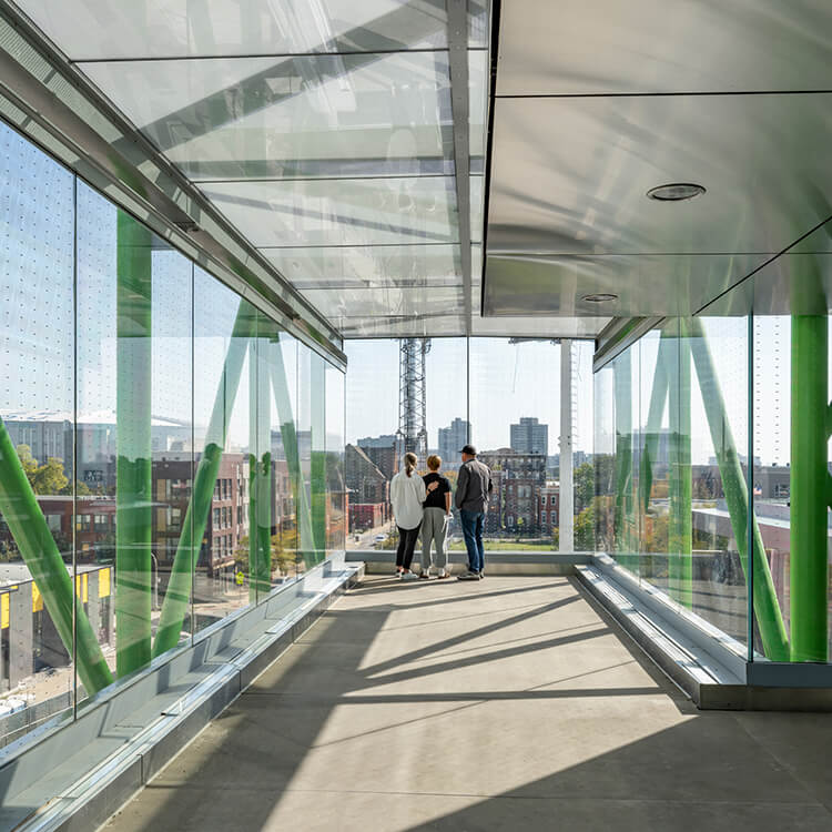 Modern urban glass walkway with three people enjoying a city view.