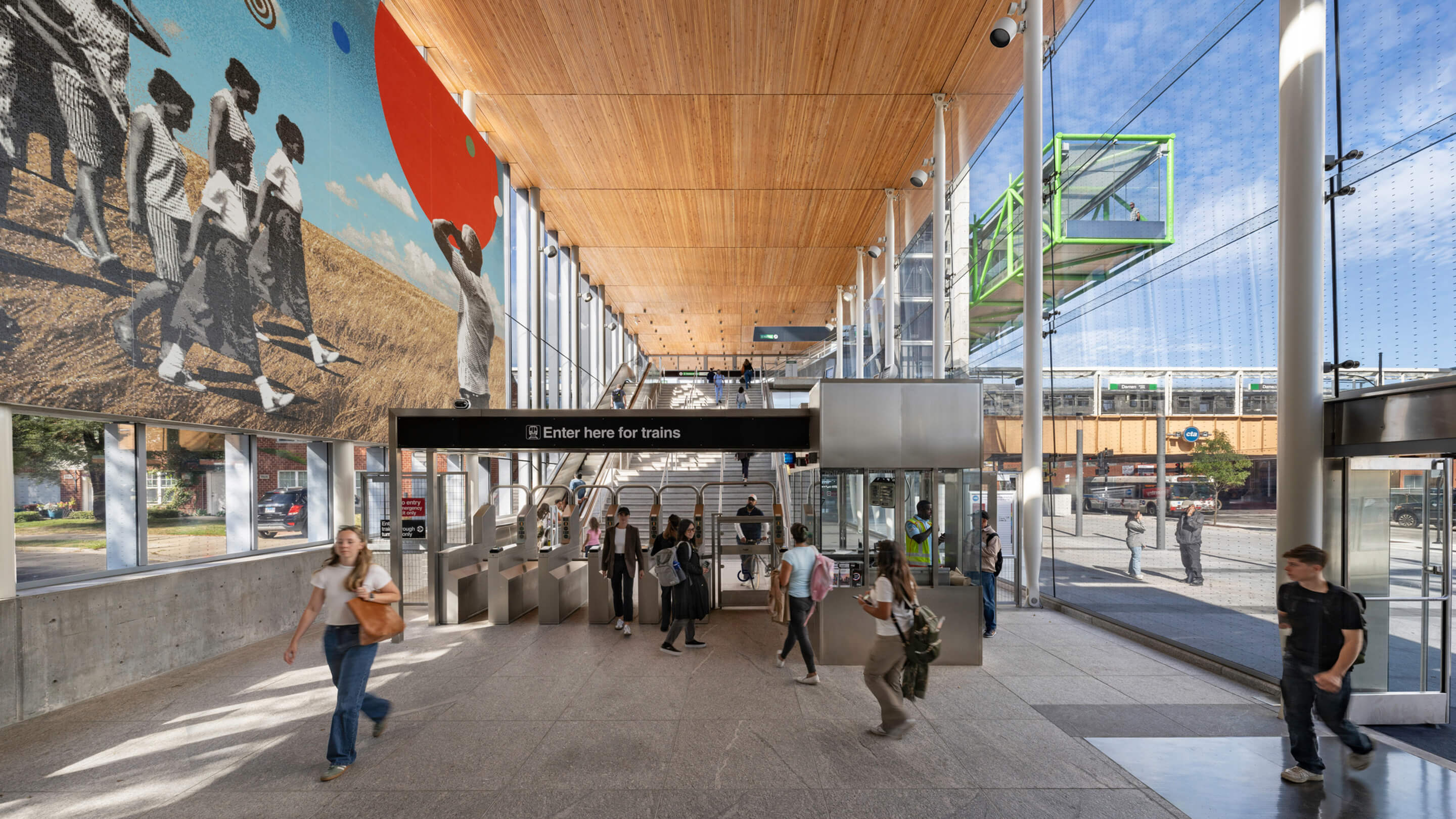 Modern train station entrance with mural and people passing through.