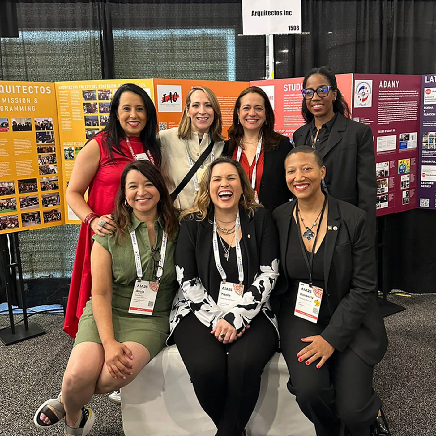 Yanel de Angel and group of women at Arquiectos Inc event booth smiling together.