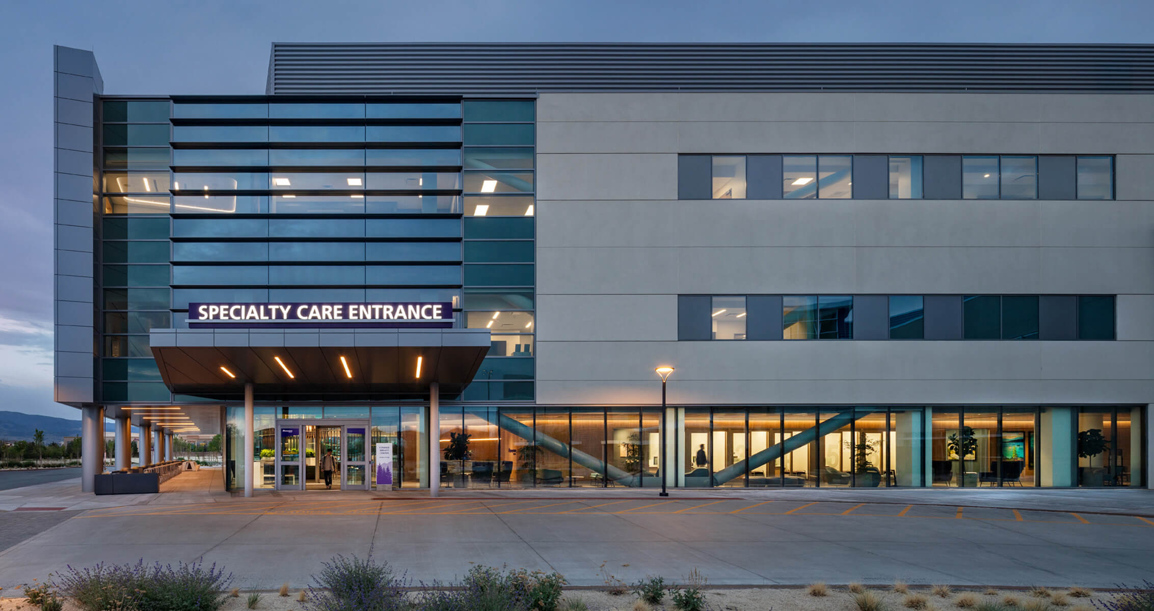 Modern specialty care entrance of medical building at dusk.