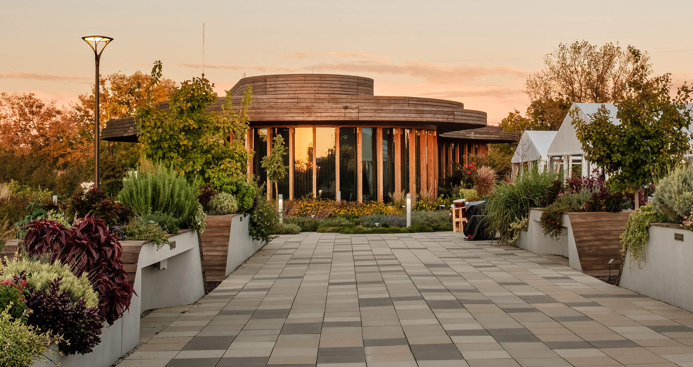 Modern garden pavilion with walkway and lush greenery at sunset.