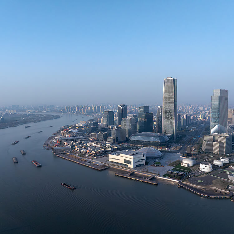 Aerial view of a modern city skyline by a river, with skyscrapers and cargo ships.