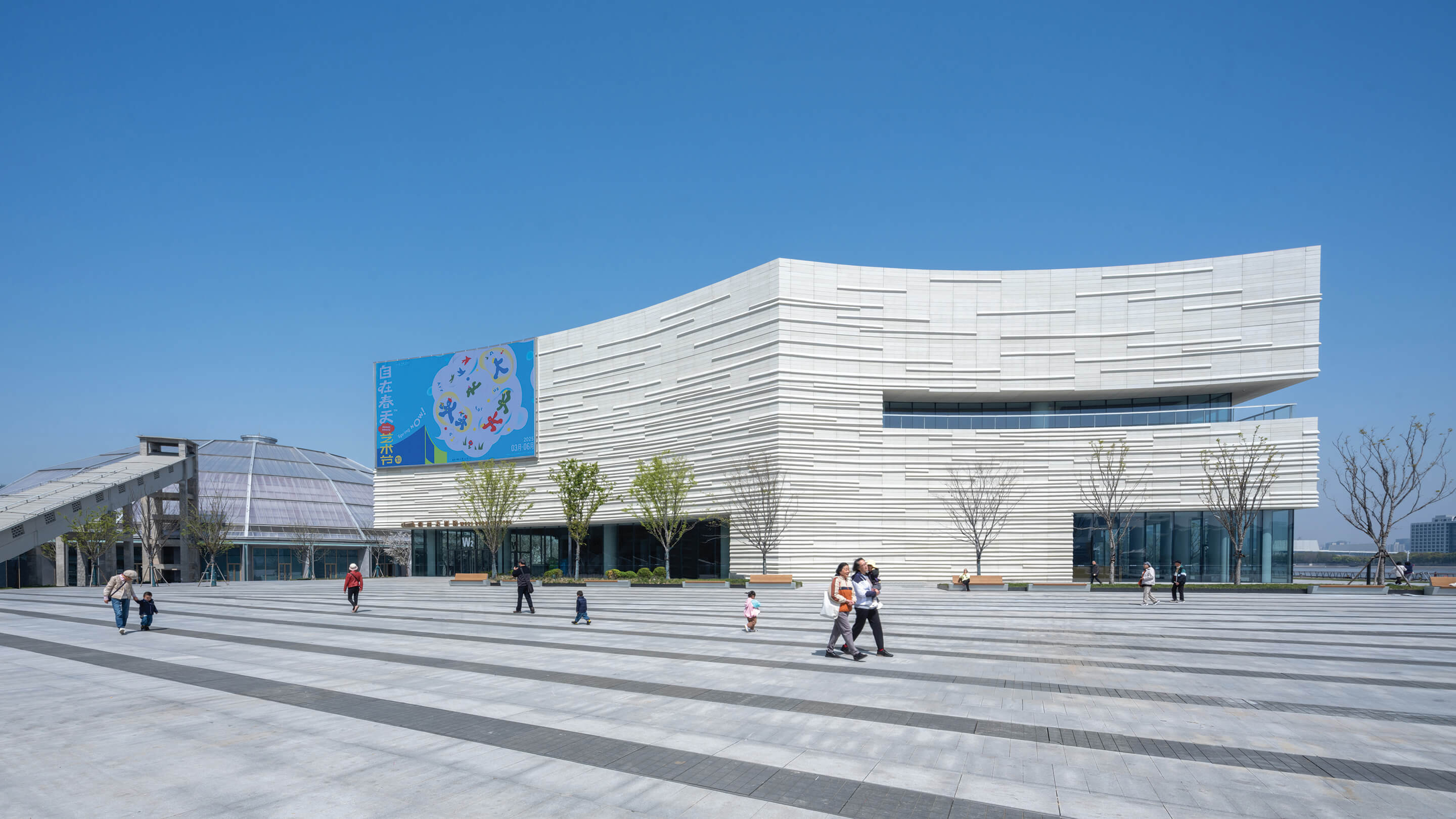 Curved building with sleek white facade and people walking outside on clear day.