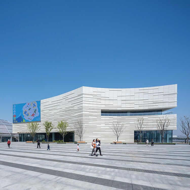 Curved building with sleek white facade and people walking outside on clear day.