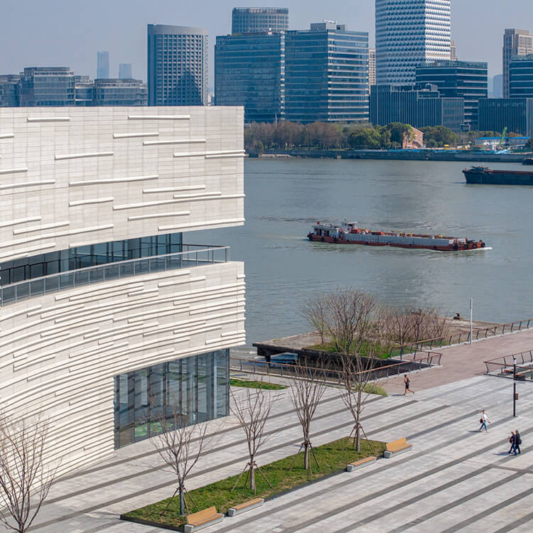 Modern riverside building with barge and cityscape in the background.
