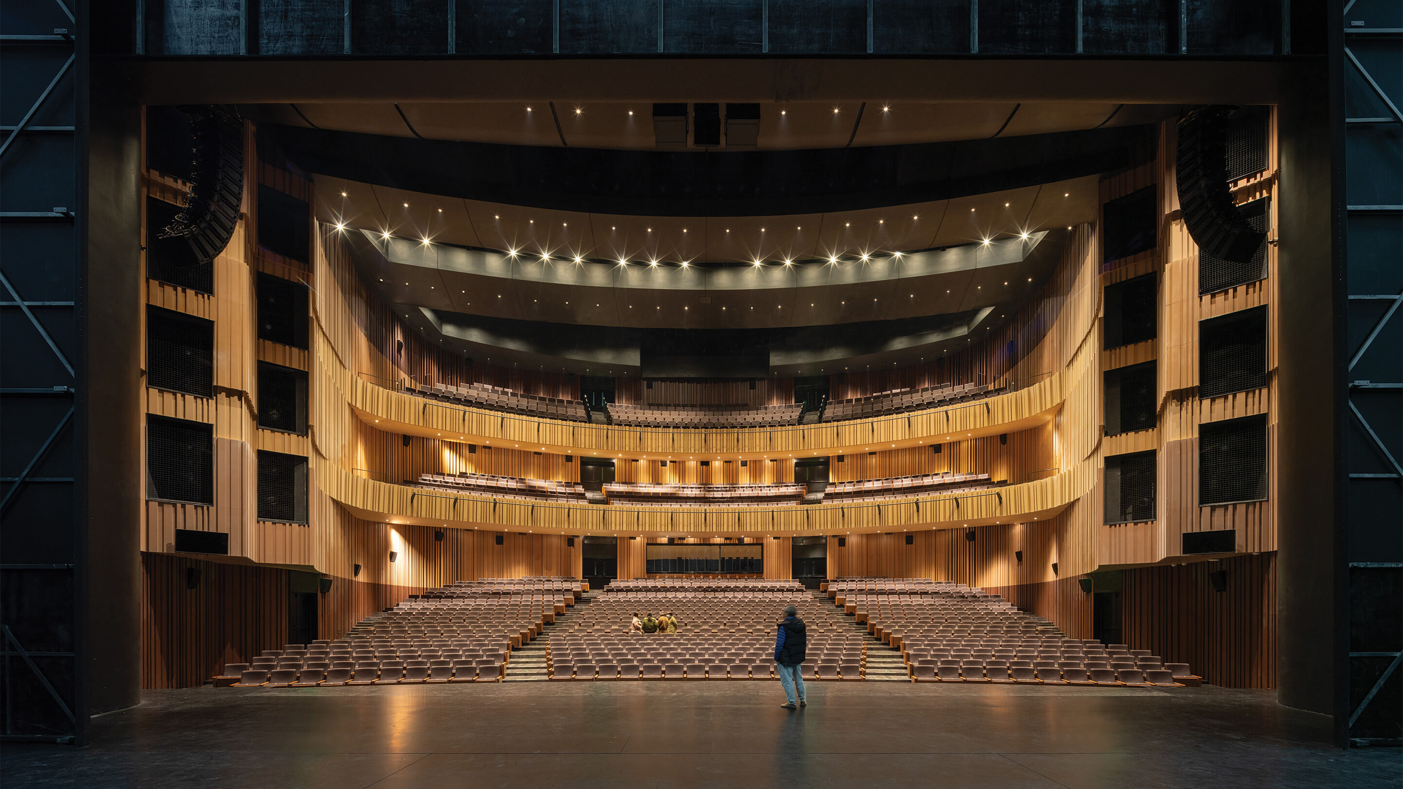 Modern theater interior from stage view, dark with warm lighting and warm-toned paneling
