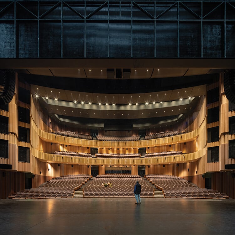 Modern theater interior from stage view, dark with warm lighting and warm-toned paneling