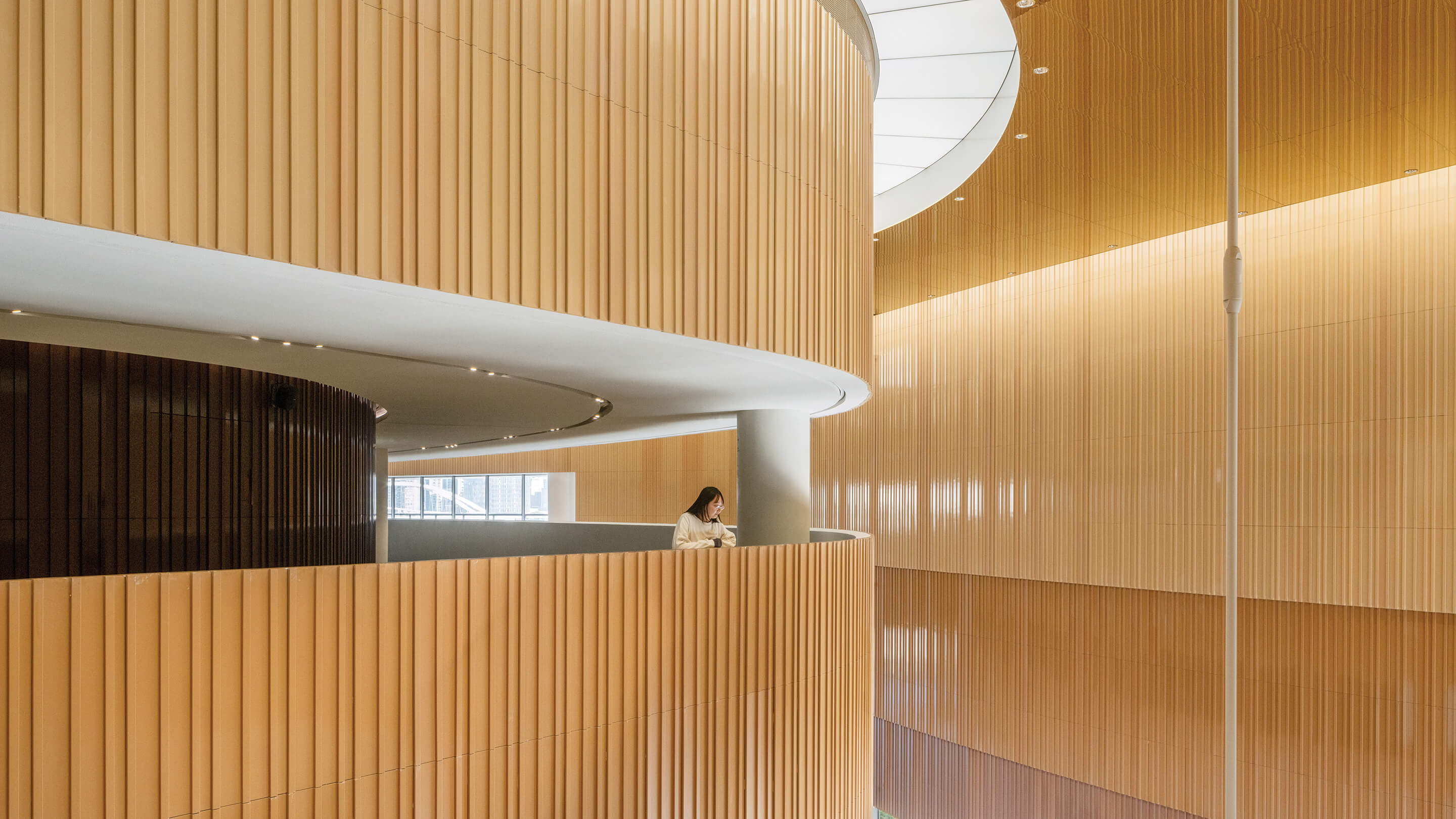 Dramatically curved interior with light wood and a person on a balcony.