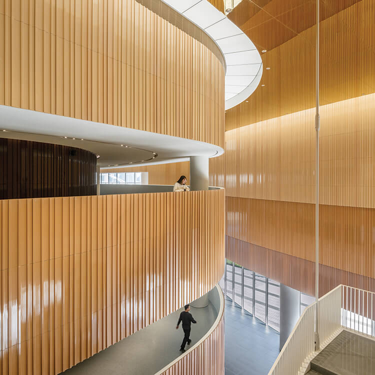 Dramatically curved interior with light wood and a person on a balcony.