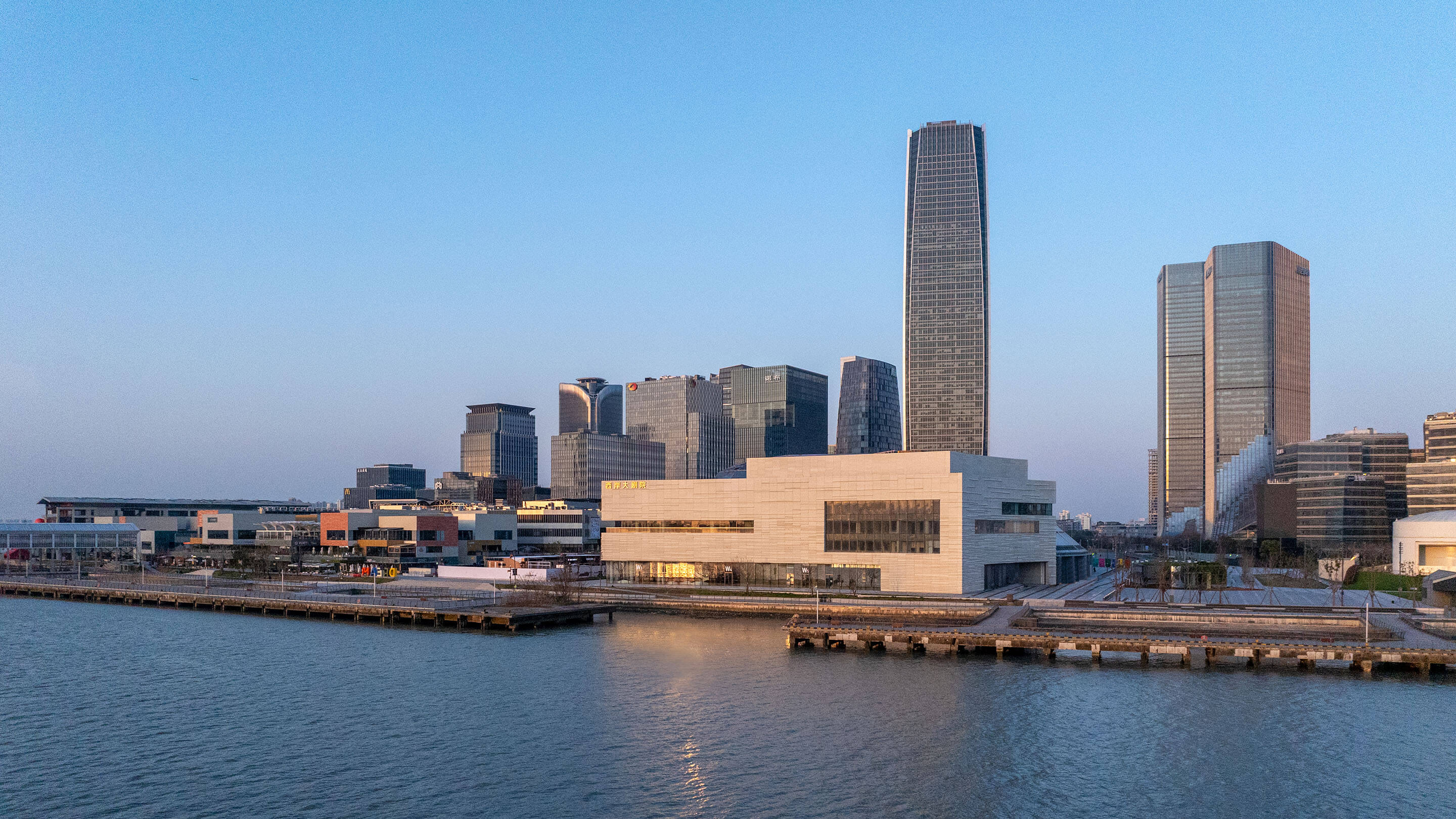 Modern skyline with waterfront buildings, including a white curved building in the center at sunset.
