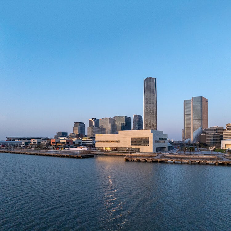 Modern skyline with waterfront buildings, including a white curved building in the center at sunset.