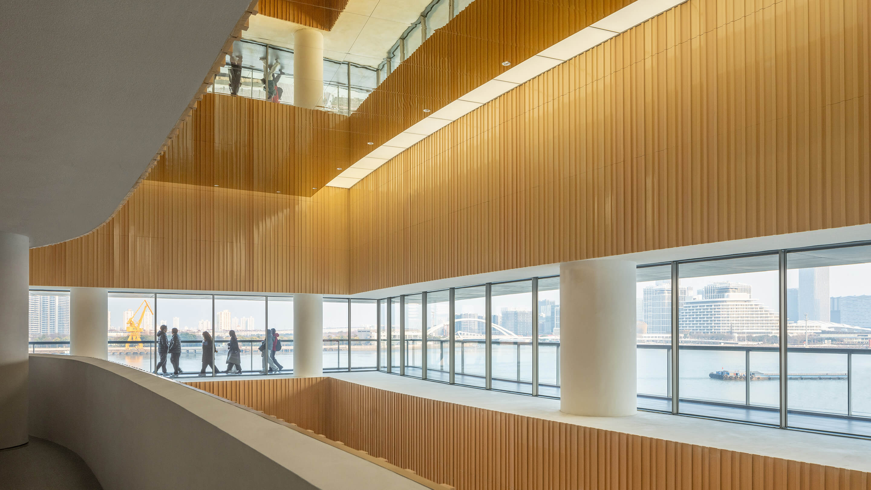 Modern building interior with people walking by large windows overlooking city skyline.