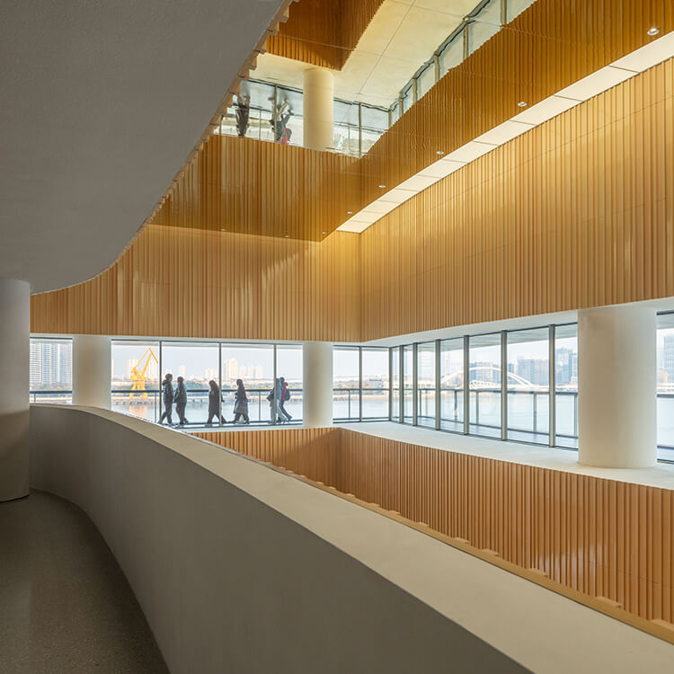 Modern interior with people walking beside large windows overlooking a cityscape.