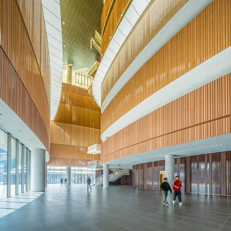 Modern architectural interior with wooden panels and high ceilings, people walking through.