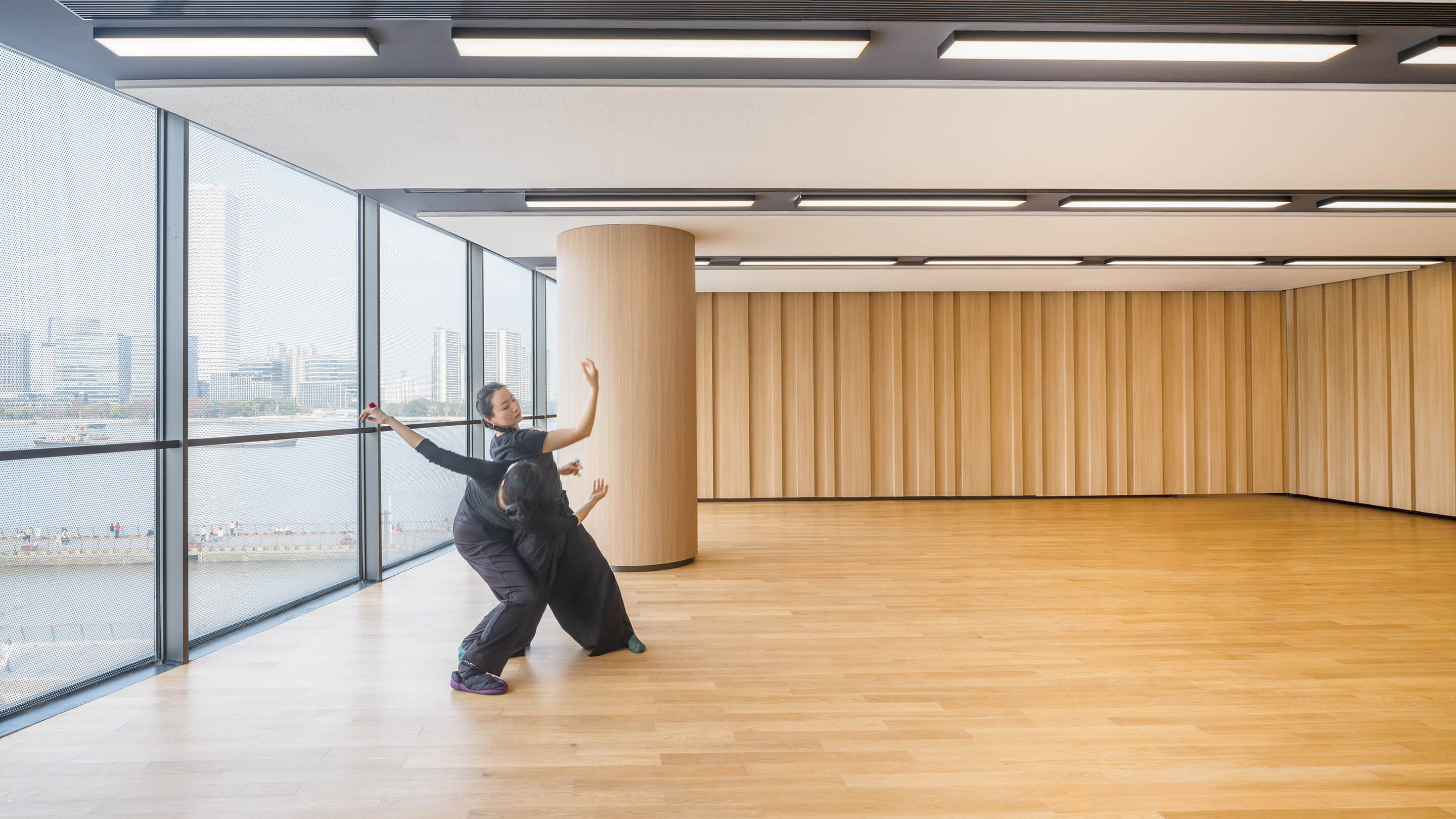 Two dancers performing in a modern studio with panoramic city views.