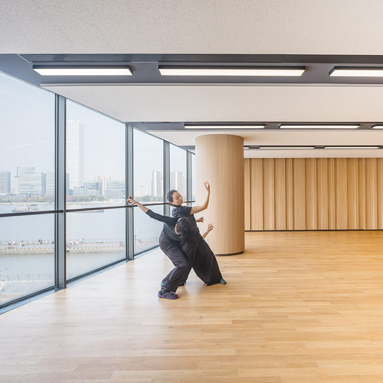 Dancers in a modern studio with cityscape view through large windows.