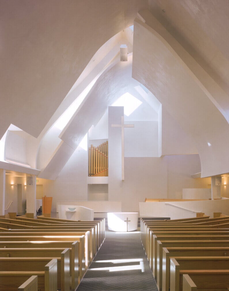 Modern church interior with wooden pews, cross, and organ pipes.