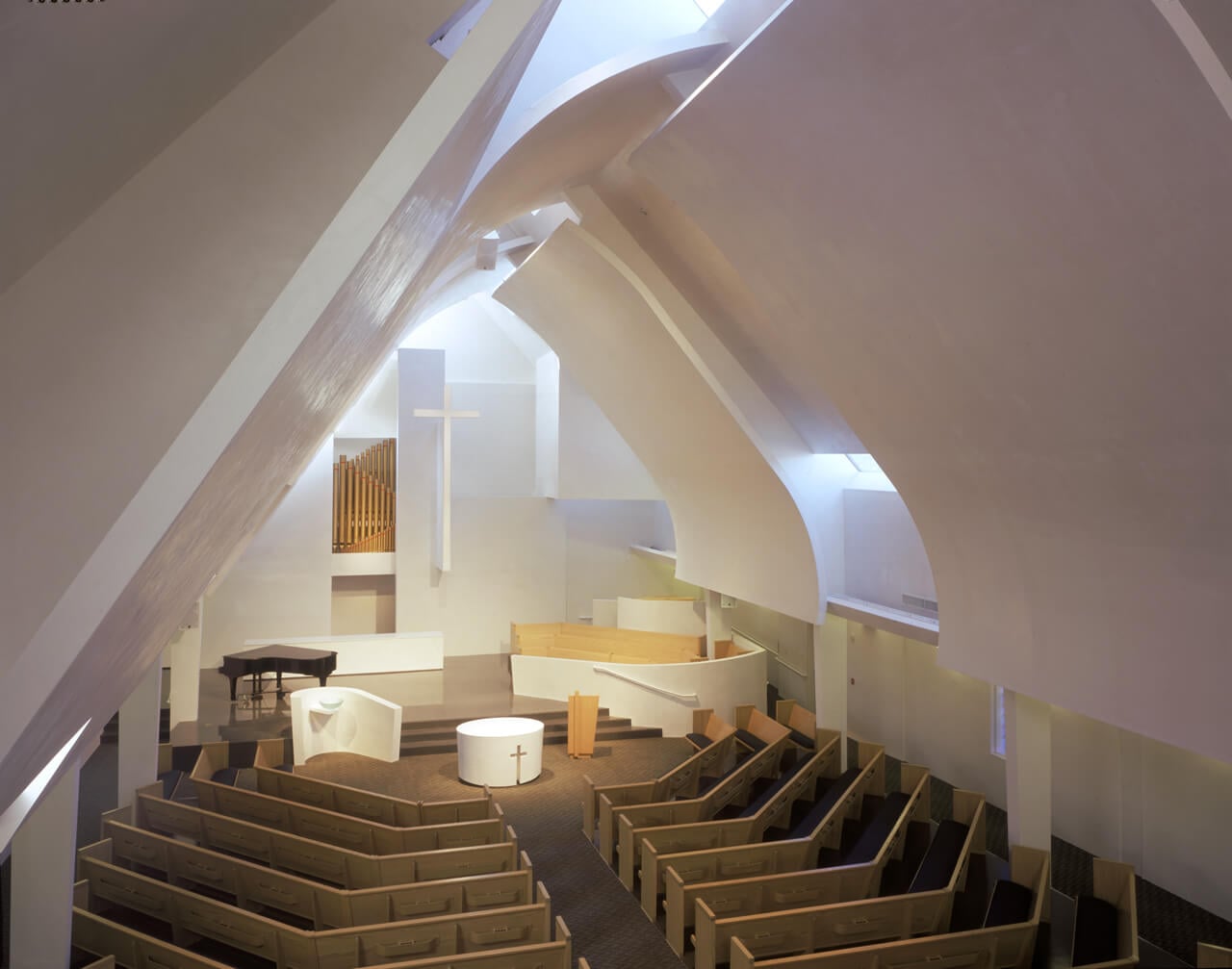 Modern church interior with curved ceiling and seating, featuring a cross and organ.