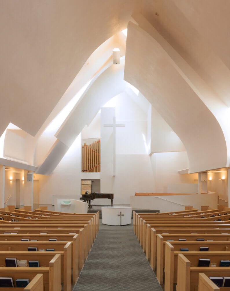Modern church interior with wooden pews and a large cross at the altar.