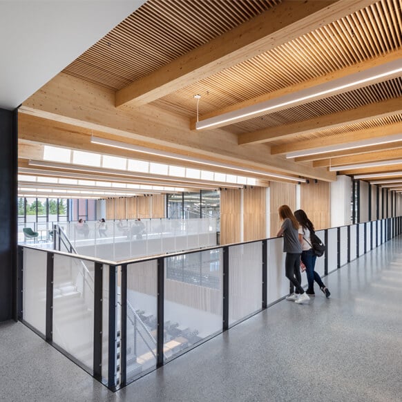 Modern hallway with wooden beams and students leaning on railing.