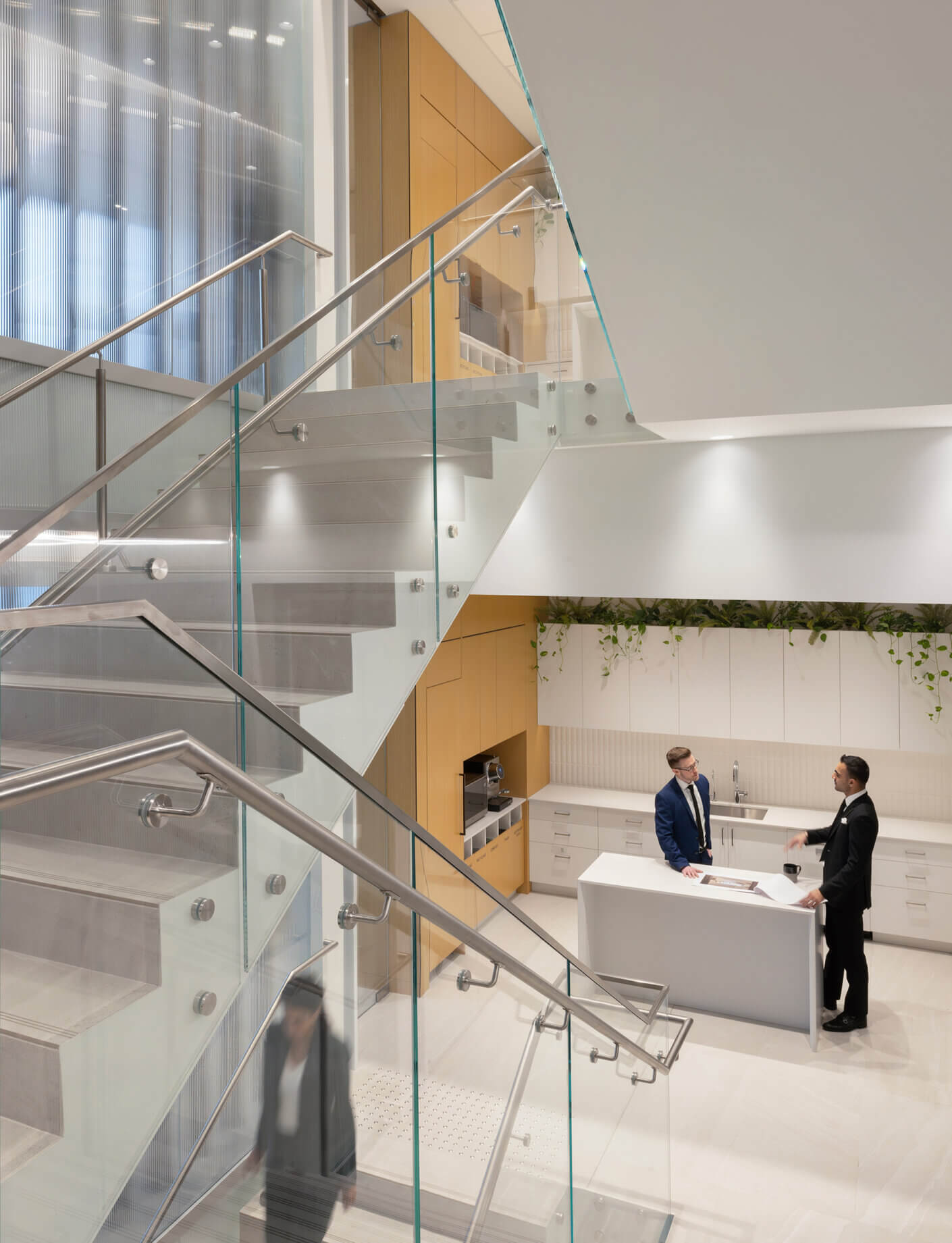 Modern office interior with glass staircase and two professionals in discussion at the counter.