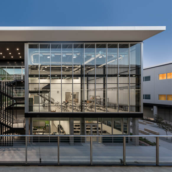 Modern glass building exterior with visible interior, showcasing office spaces at dusk.