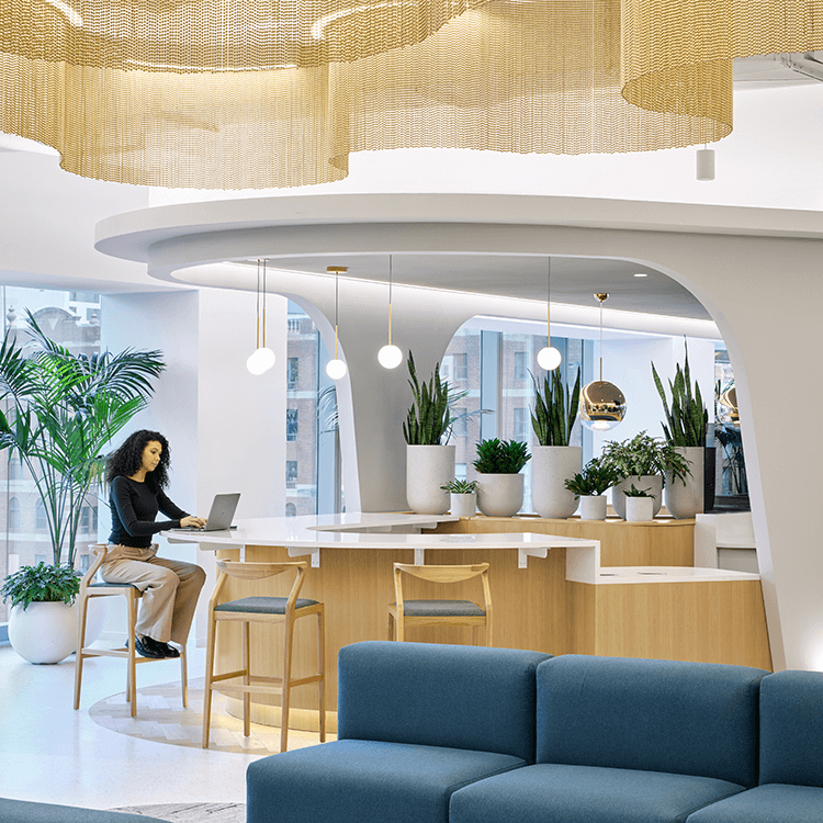 Modern coworking space with plants, seating, and a person working on a laptop.