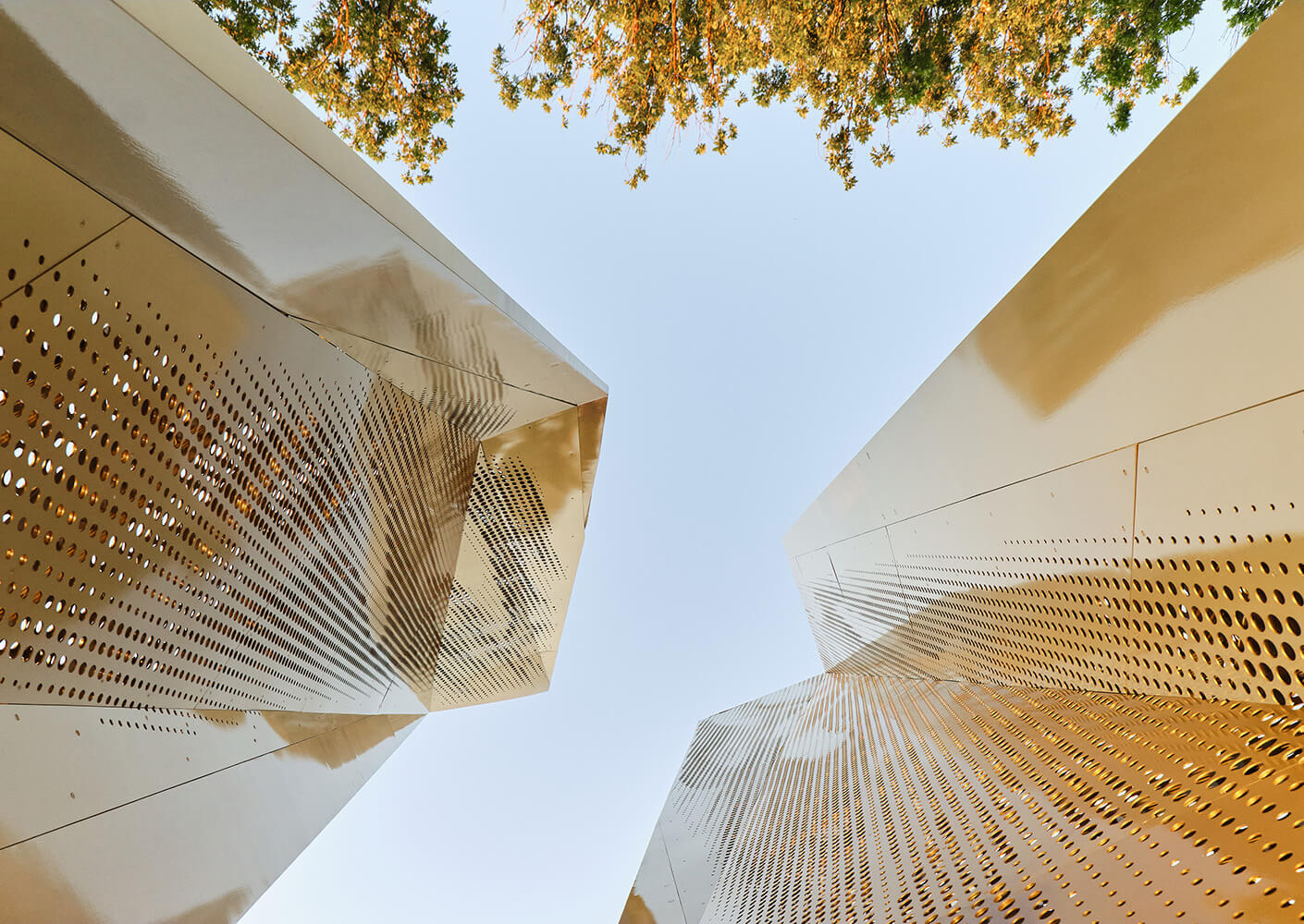 Modern architectural structures with perforated metallic panels under a blue sky.