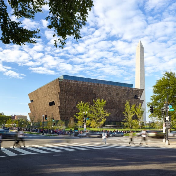 Contemporary museum with landmark obelisk under a vibrant sky, busy street in foreground.