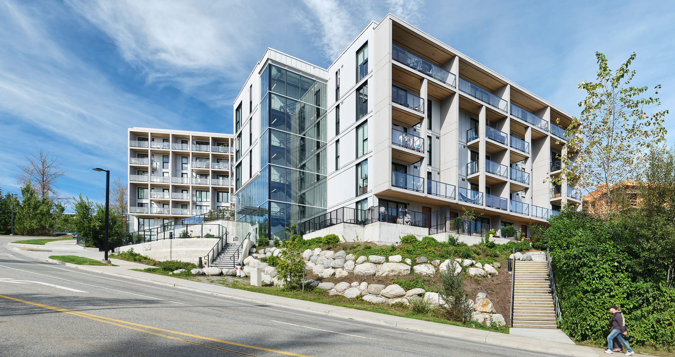 Modern apartment building with glass balconies and lush surroundings under a clear blue sky.