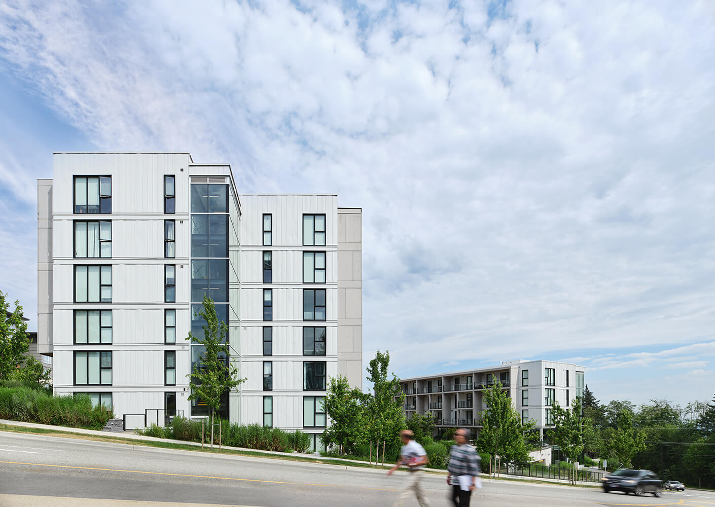 Modern apartment buildings under cloudy sky with pedestrians in the foreground.