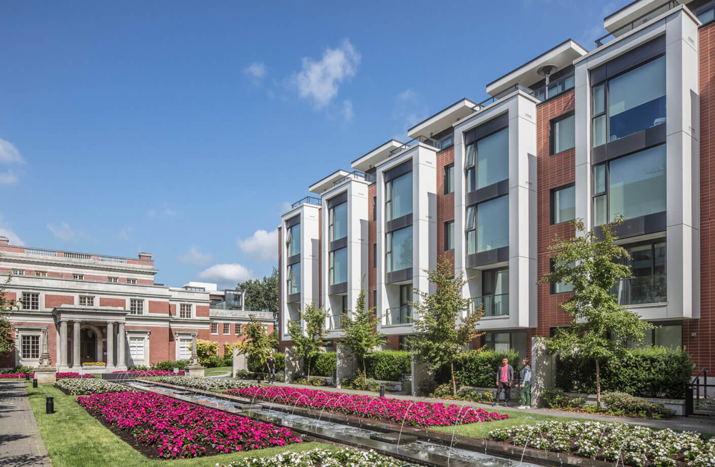 Modern building with gardens and fountain under a clear blue sky.