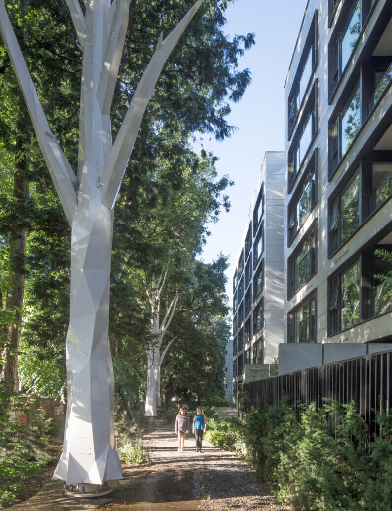 Modern architecture and nature blend along a tree-lined path with two people walking.