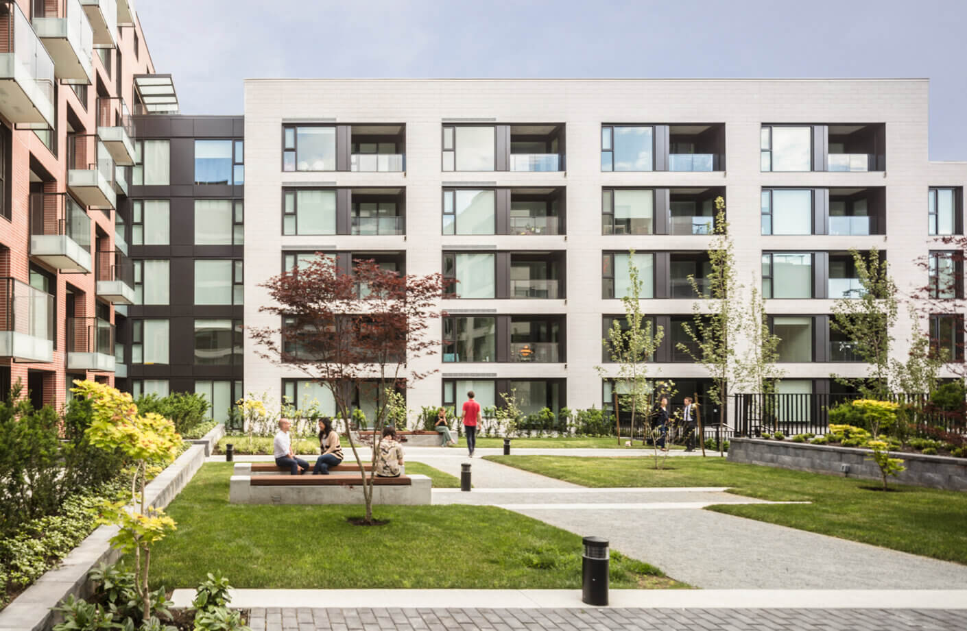 Modern apartment complex with landscaped courtyard and people relaxing on benches.