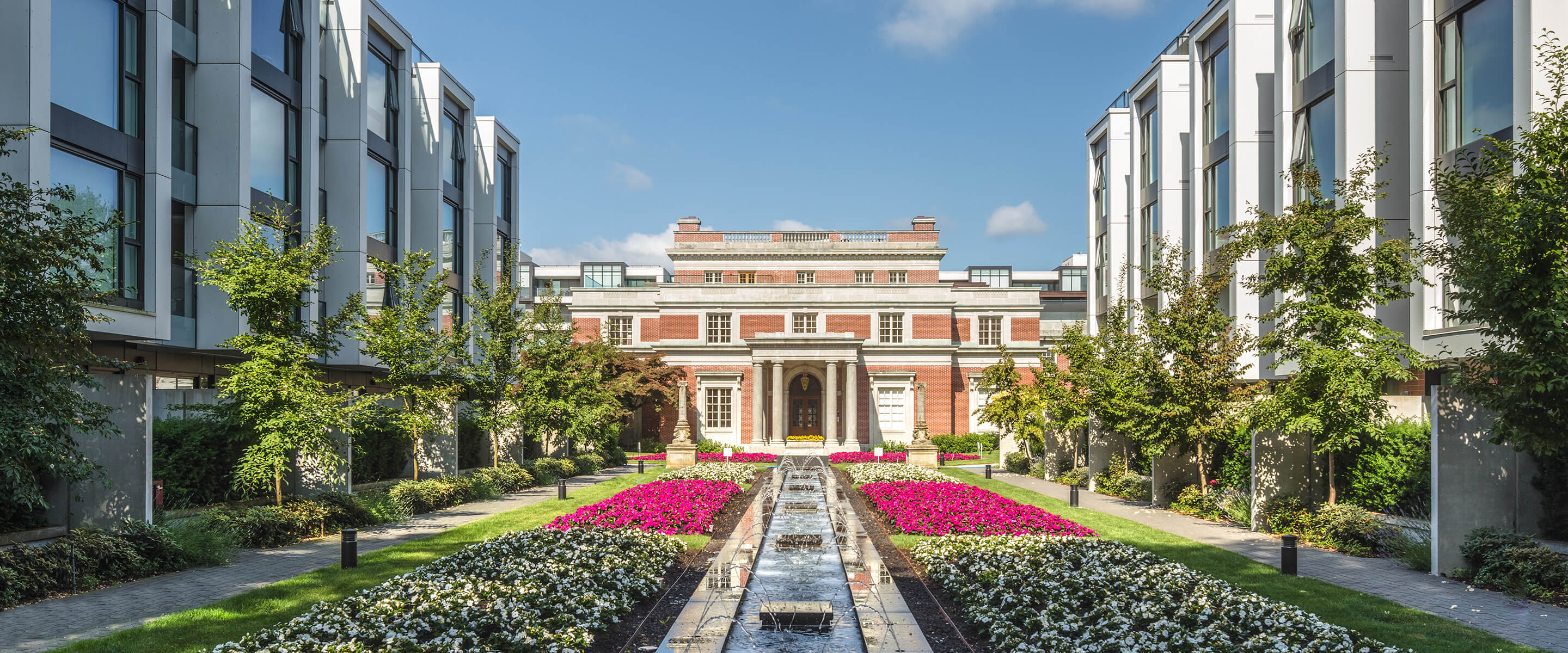 Modern building facade and garden with fountain and flowers under a clear blue sky.