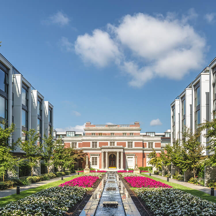 Elegant building with symmetrical garden and fountain under blue sky.