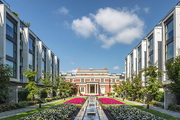 Modern campus with manicured gardens and classic brick building under a blue sky.