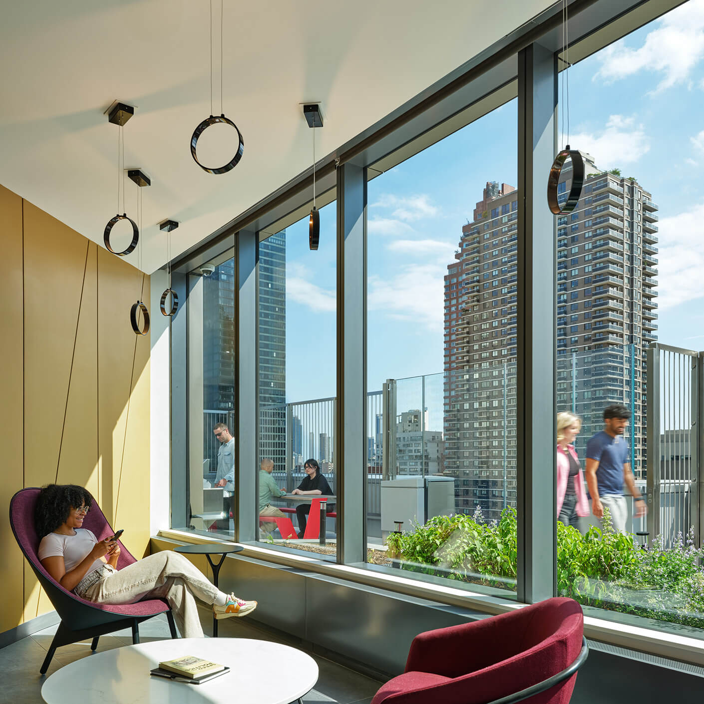 Student residence lounge with city skyline view, people relaxing and working near large windows.
