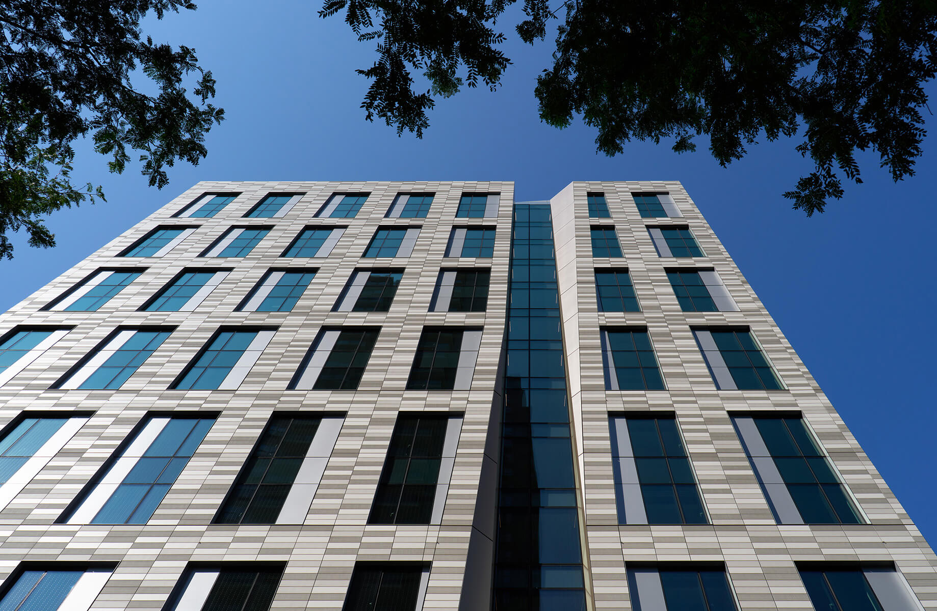 Student residence building exterior with tall glass windows against blue sky.