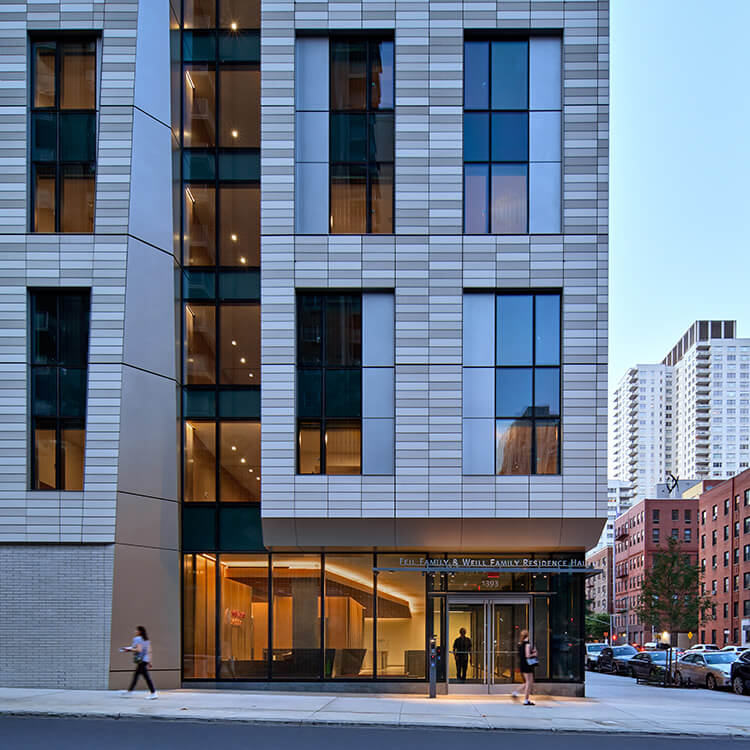 Student residence building with glass windows and street view at dusk.