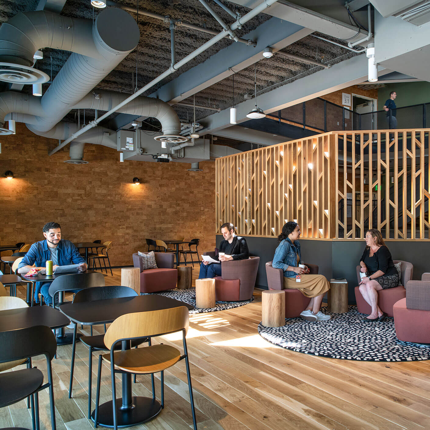 Modern office lounge with people working and socializing. Cozy seating and wooden decor accents.