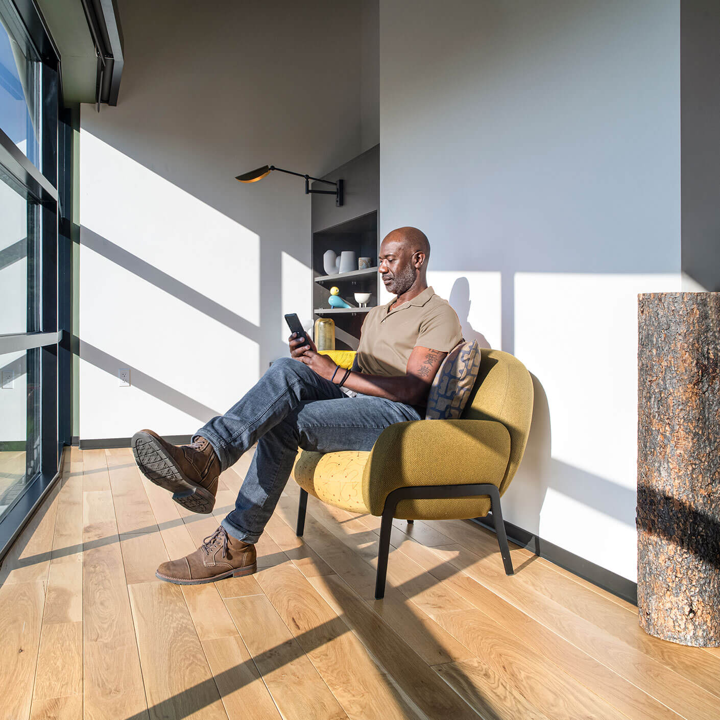 Man sitting in a sunny room, using a smartphone on a yellow chair.