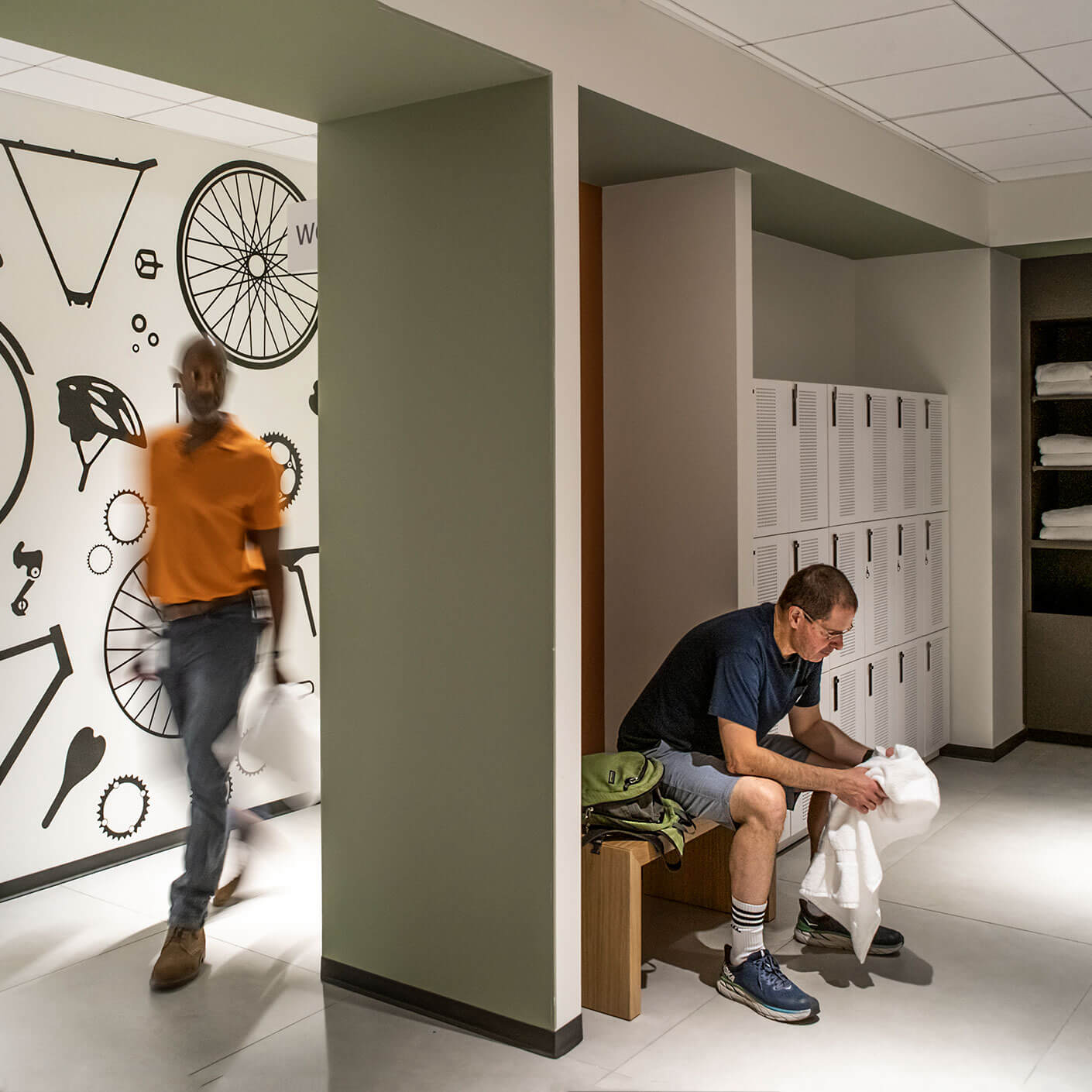 Locker room with bicycle-themed wall and men using lockers and benches.