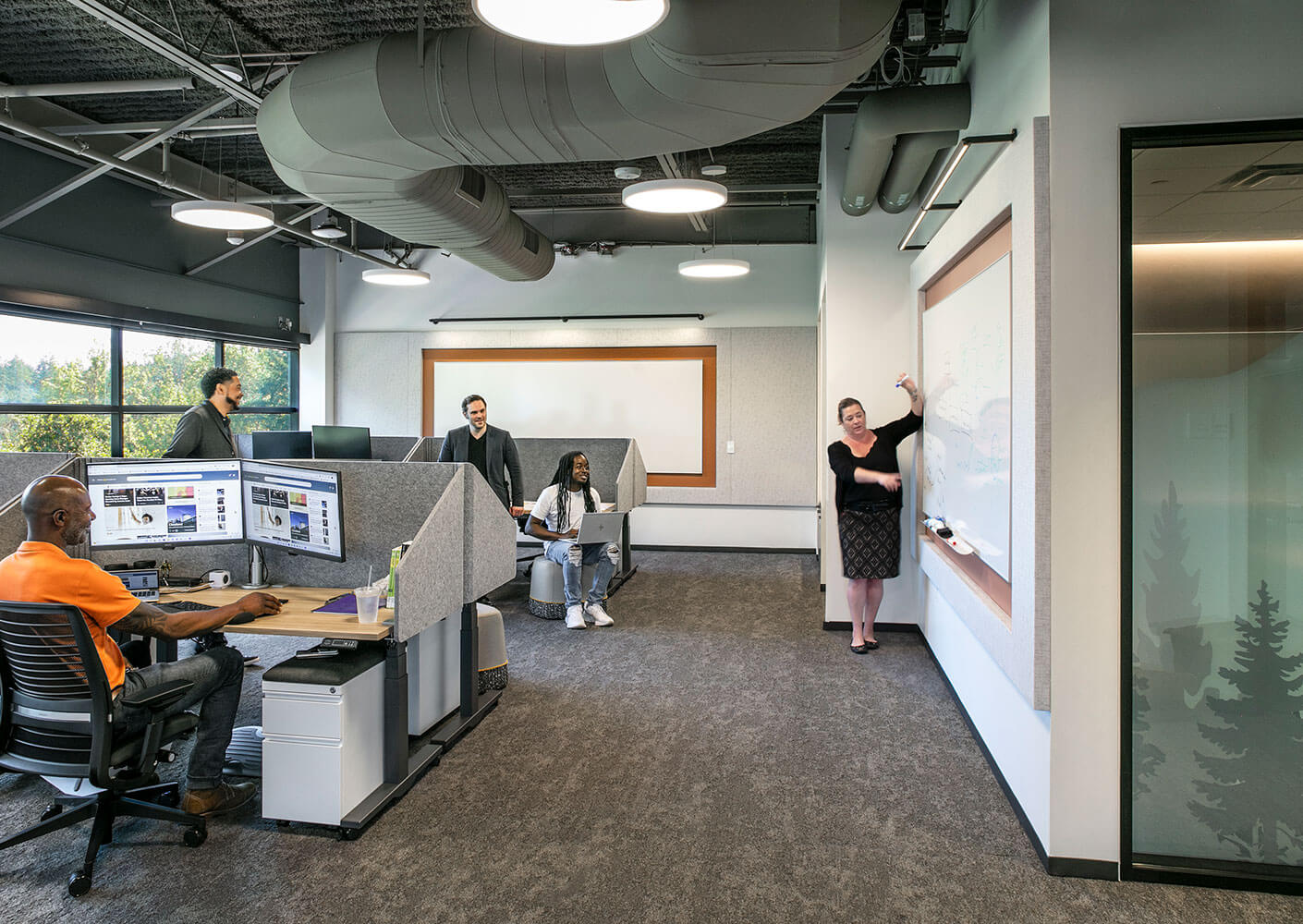 Modern office with team collaborating, working at desks and using a whiteboard.