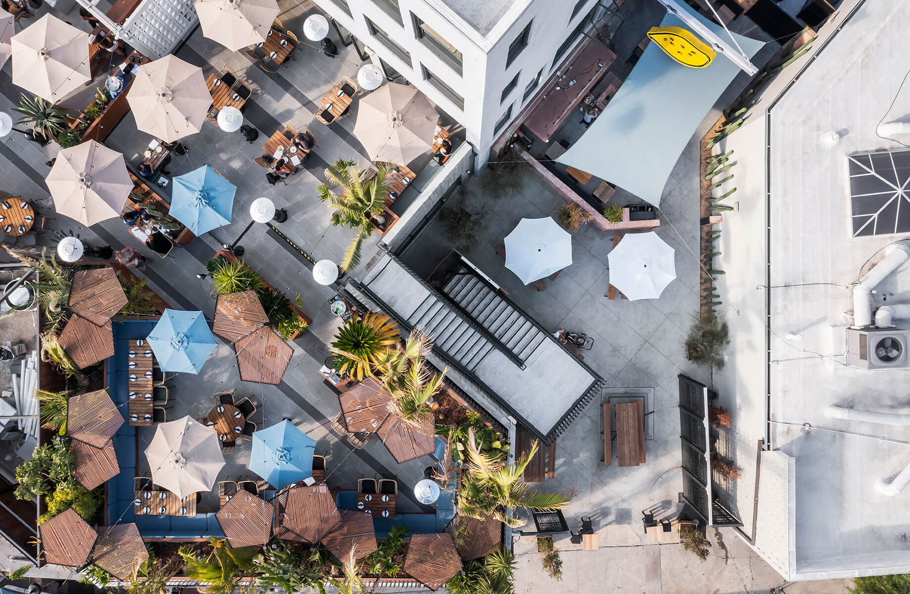 Aerial view of outdoor dining with umbrellas and greenery on a rooftop terrace.