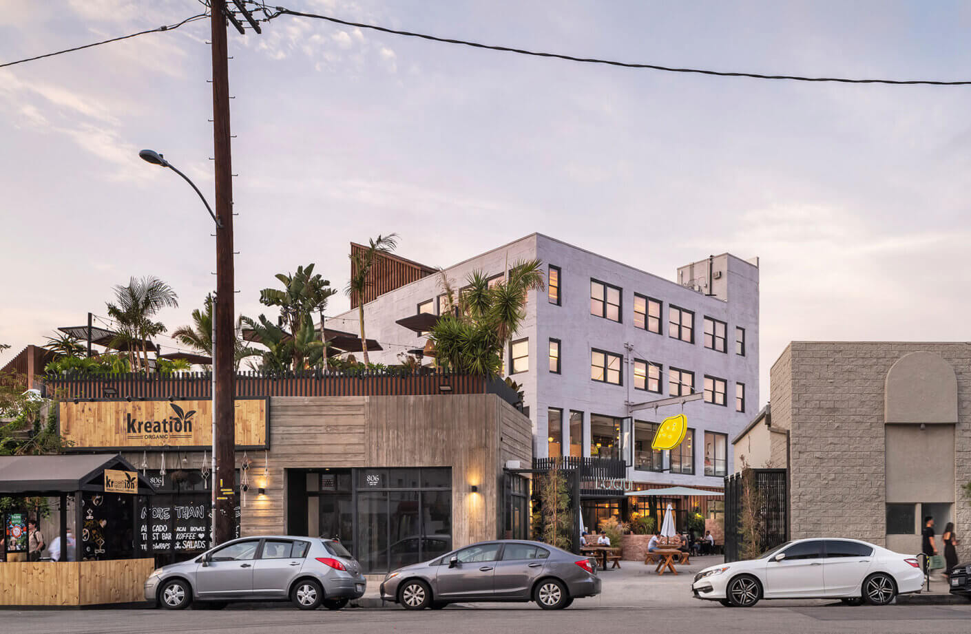 Urban street view with outdoor cafe and modern building at sunset.