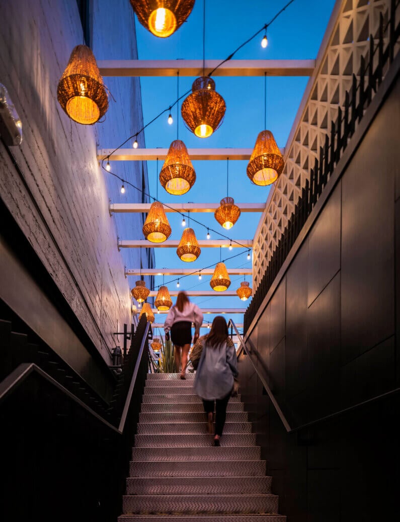 Two people ascending lit outdoor staircase with hanging lanterns.