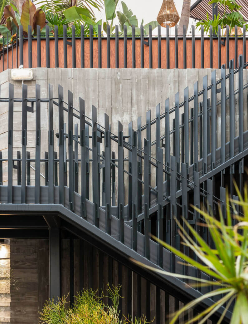 Modern metal staircase with unique railing design, surrounded by lush greenery.